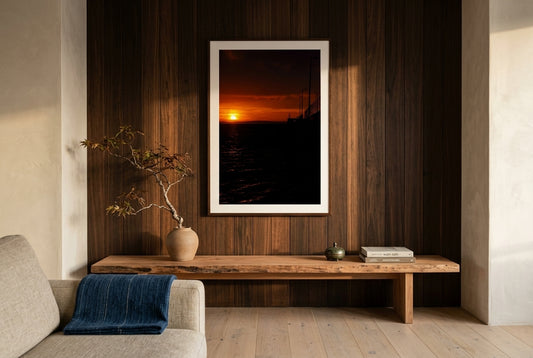 Golden Dawn at Flinders Pier, framed above a low cedar mantel-console in a refined Australian-Japanese fusion living room — ikebana arrangement, cedar feature wall, oat linen sofa glimpse, dark wood frame. — Two Fat Bunnies.