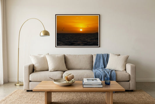 Golden Sunset Over Port Phillip Bay, framed above an oat-linen sofa in a Mornington beach house living room — cream linen cushions, soft blue throw, jute rug, brass arc lamp, dark wood frame. — Two Fat Bunnies.