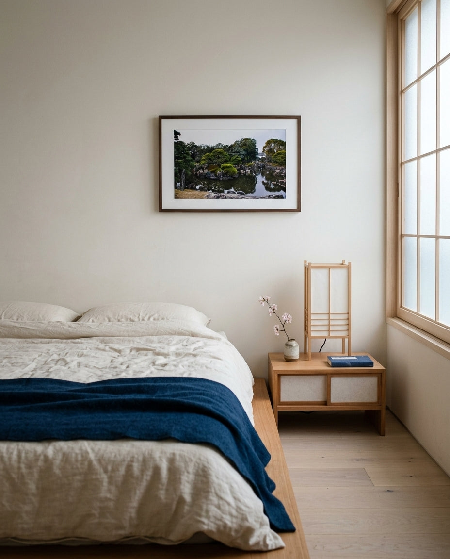 Serenity in Stone: Japanese Garden at Nijo Castle, Kyoto, framed above a low Japanese platform bed — cream linen bedding, indigo throw, paper-shaded bedside lamp, dark wood frame. — Two Fat Bunnies.