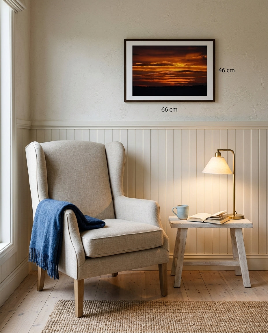 Sunrise over Bass Strait: Dawn at Flinders, framed above a linen reading chair in a seaside reading corner — woven wool throw, oak side table, ceramic mug, stack of photography books, dark wood frame. — Two Fat Bunnies.
