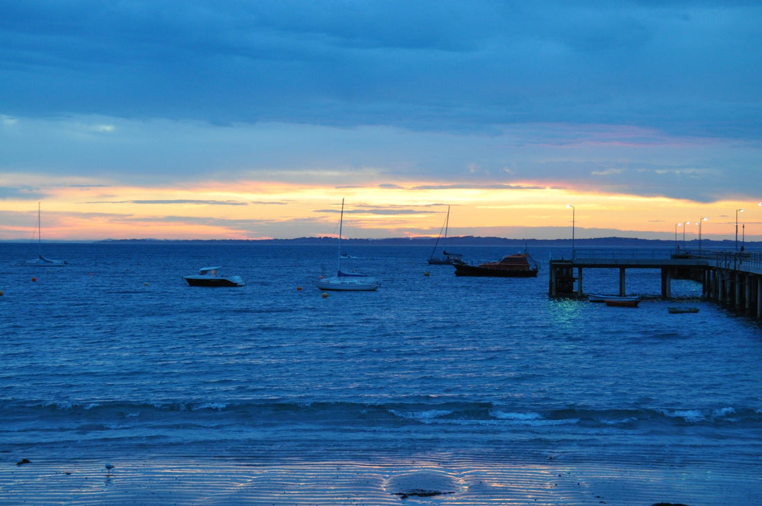 Pre-sunrise blue hour at Flinders Pier — boats silhouetted on dark water, warm band of light on the horizon over Bass Strait, Mornington Peninsula