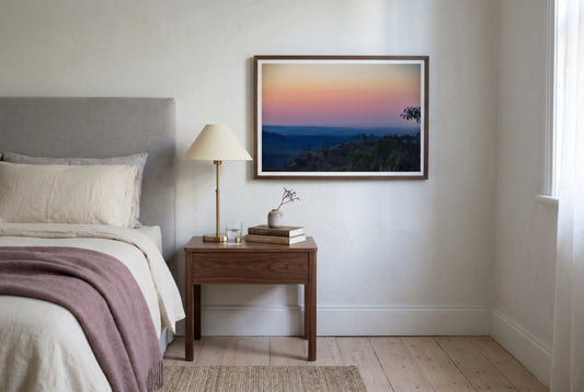 Afterglow over El Questro, Pastel Twilight from Buddy's Lookout, framed above a walnut bedside table in a Melbourne bedroom — dove-grey linen headboard, brass reading lamp, layered linen bedding, dark wood frame. — Two Fat Bunnies.
