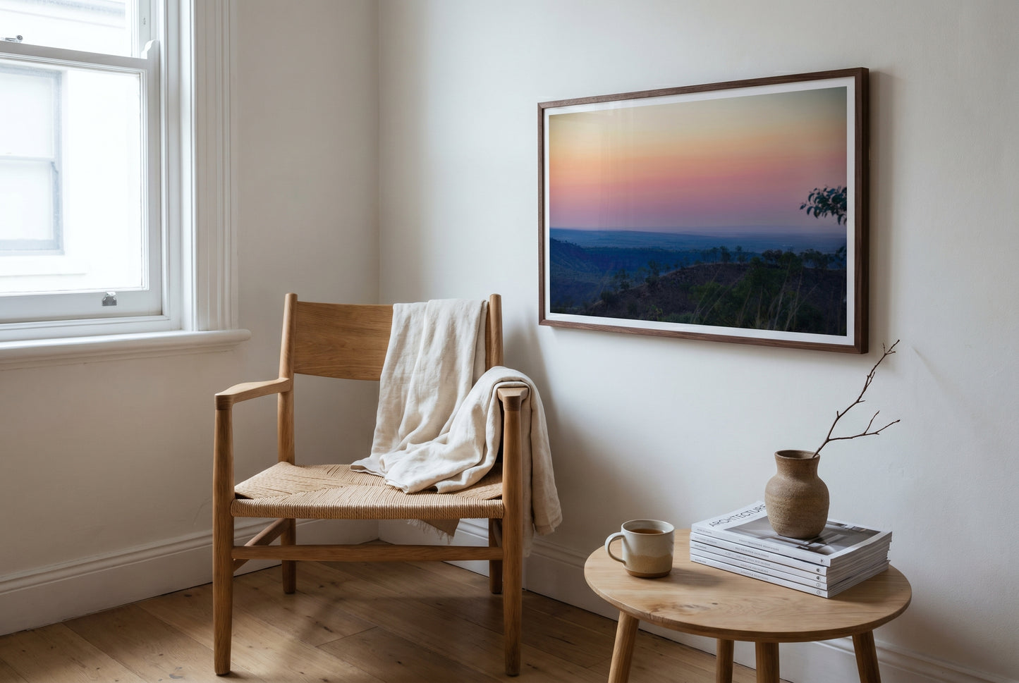 Afterglow over El Questro, Pastel Twilight from Buddy's Lookout, framed beside an oak Wegner-style reading chair in a Sydney apartment — cream linen throw, side table, ceramic vessel, dark wood frame. — Two Fat Bunnies.