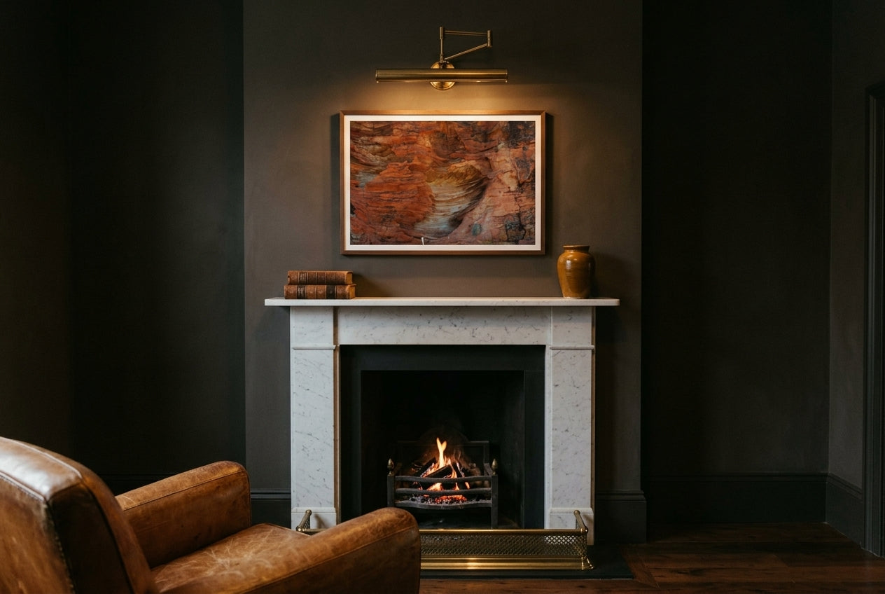 Beehive Patterns, framed above a slim white-marble fireplace mantel in an intimate charcoal snug — brass fender, ember fire, leather club chair, dark wood frame. — Two Fat Bunnies.