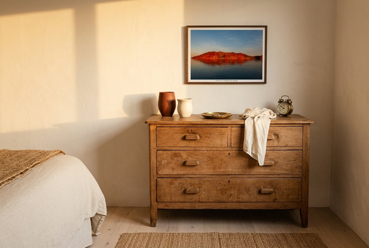 Crimson Calm — Island Before Sunset, Lake Argyle, framed above a vintage oak dresser in a master bedroom — terracotta and cream ceramics, ivory linen, antique alarm clock, dark wood frame. — Two Fat Bunnies.