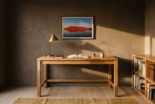 Crimson Calm — Island Before Sunset, Lake Argyle, framed above a solid raw-oak writing desk in a warm Australian study — deep mushroom plaster, brass-shaded reading lamp, faded ochre kilim, dark wood frame. — Two Fat Bunnies.
