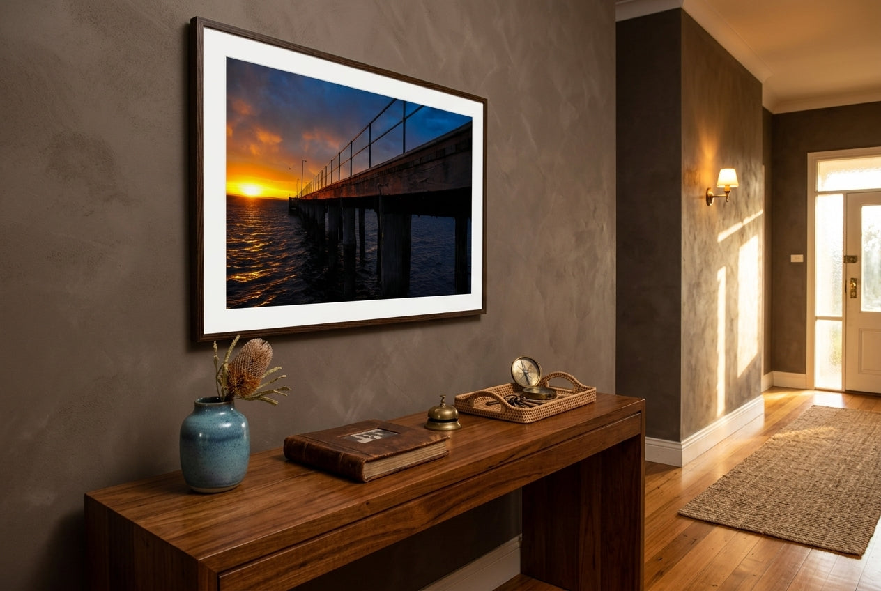 Dawn at Flinders Pier, framed above a generous blackbutt console in a Mornington Peninsula heritage entry hall — deep mushroom plaster, coastal-blue ceramic vessel, polished blackbutt floors, brass sconce, dark wood frame. — Two Fat Bunnies.