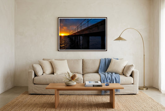 Dawn at Flinders Pier, framed above an oat-linen sofa in a refined Mornington Peninsula beach house living room — woven cream cushions, soft blue throw, jute rug, brass arc lamp, dark wood frame. — Two Fat Bunnies.