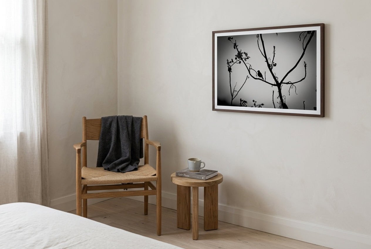 Dusk Solitude — El Questro Bird Silhouette, framed beside a single oak Wegner-style reading chair in a contemplative master bedroom corner — charcoal wool throw, side table, hardback book, ceramic mug, dark wood frame. — Two Fat Bunnies.