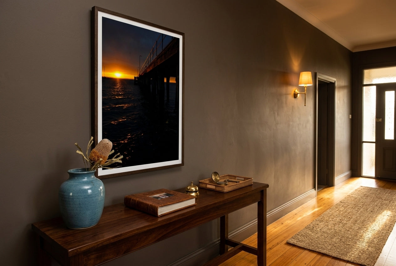Flinders Sunrise Glow, framed above a generous blackbutt console in a Mornington heritage entry hall — deep mushroom plaster, coastal-blue ceramic, polished blackbutt floors, brass sconce, dark wood frame. — Two Fat Bunnies.