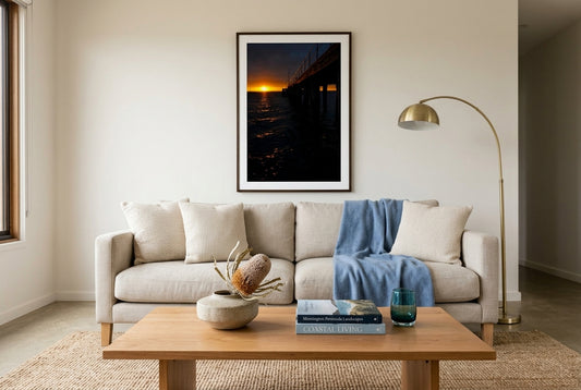 Flinders Sunrise Glow, framed above an oat-linen sofa in a refined Mornington beach house living room — cream linen cushions, soft blue throw, jute rug, brass arc lamp, dark wood frame. — Two Fat Bunnies.