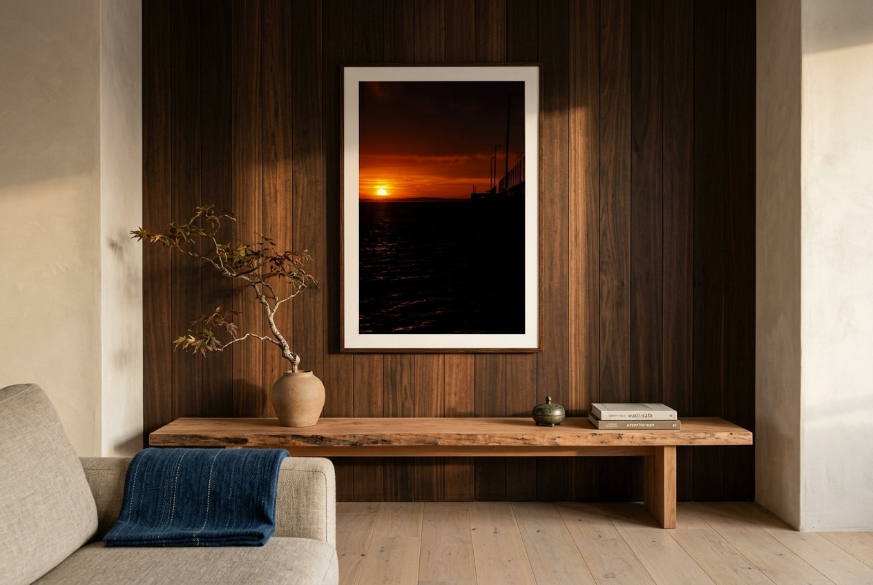 Golden Dawn at Flinders Pier, framed above a low cedar mantel-console in a refined Australian-Japanese fusion living room — ikebana arrangement, cedar feature wall, oat linen sofa glimpse, dark wood frame. — Two Fat Bunnies.