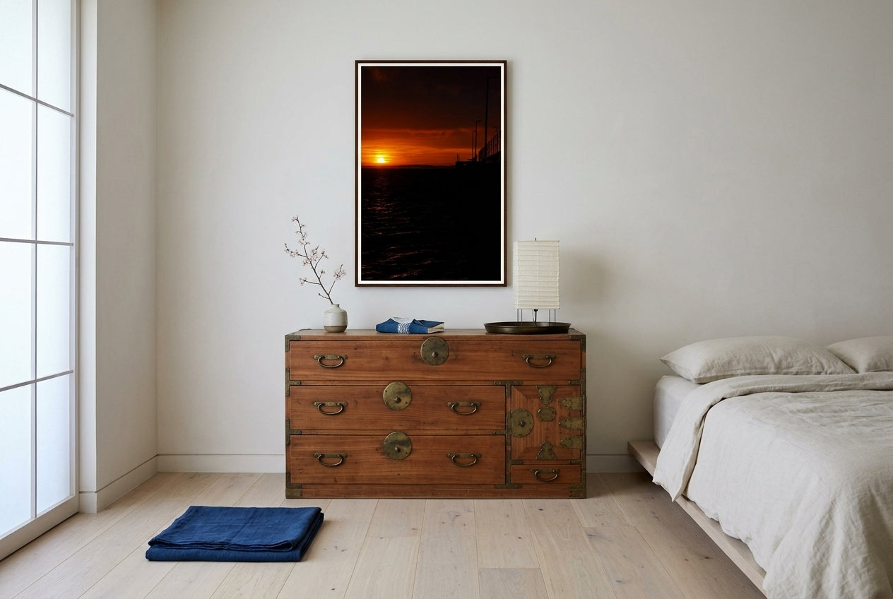 Golden Dawn at Flinders Pier, framed above a Japanese tansu chest in a Japandi master bedroom — cream linen platform bed, indigo throw, paper lamp, dark wood frame. — Two Fat Bunnies.