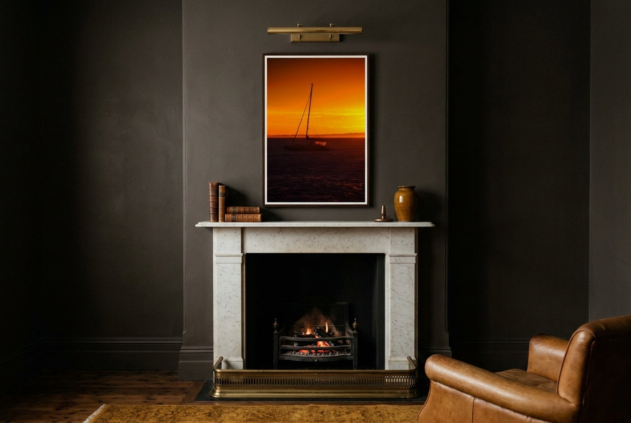 Golden Dawn at Flinders – Sunrise Boat, framed above a charcoal snug mantelpiece — brass fender, low ember fire, leather club chair, dark wood frame. — Two Fat Bunnies.