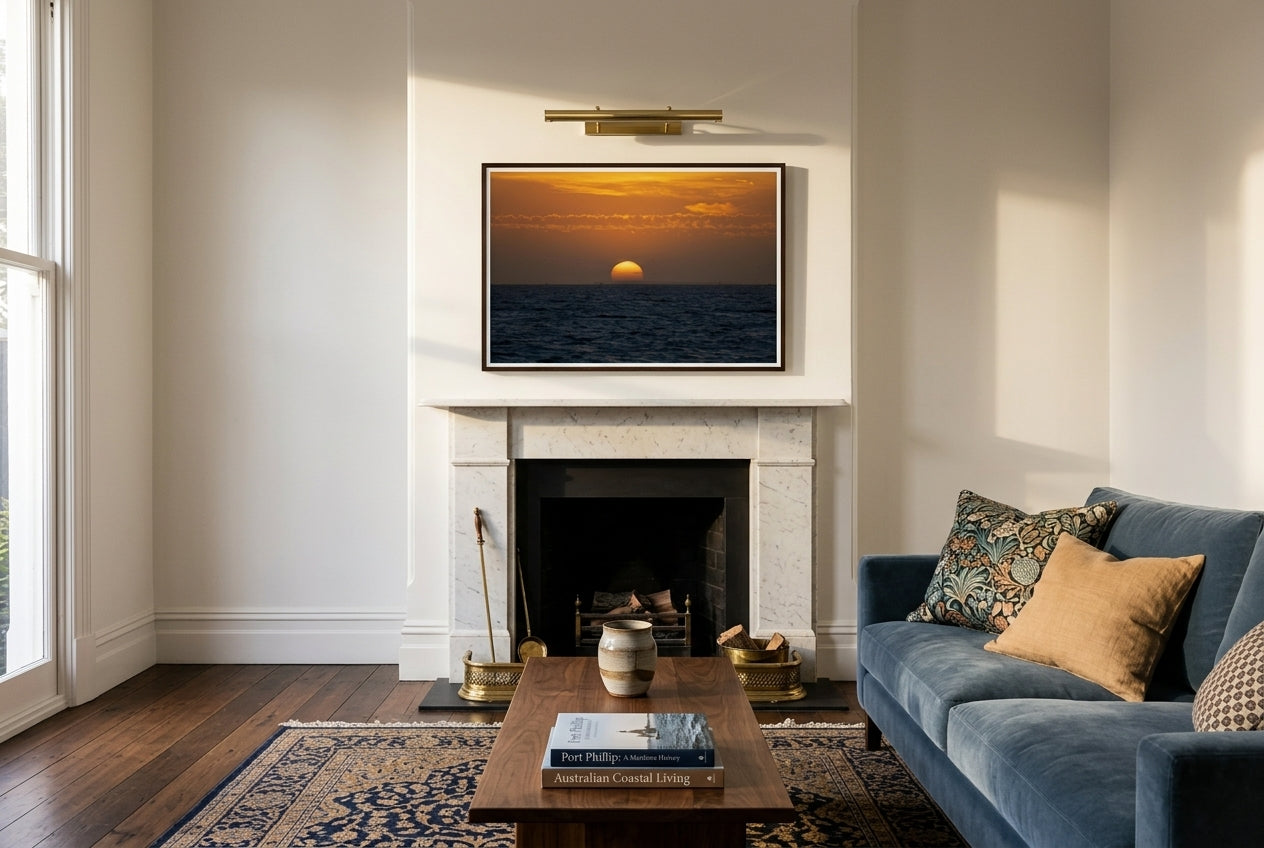 Golden Dusk: Sunset Over Port Phillip Bay, Melbourne, framed centered above a white-marble fireplace mantel in a formal Melbourne living room — dusty-blue velvet sofa, oriental rug, dark wood frame. — Two Fat Bunnies.