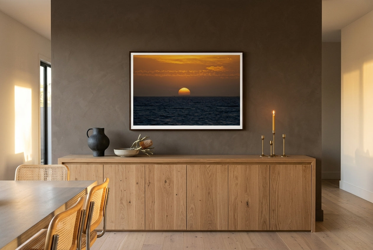 Golden Dusk: Sunset Over Port Phillip Bay, Melbourne, framed above a long raw-oak sideboard in an open-plan Australian living-dining space — sculptural ceramics, brass candleholders, dried banksia, dark wood frame. — Two Fat Bunnies.