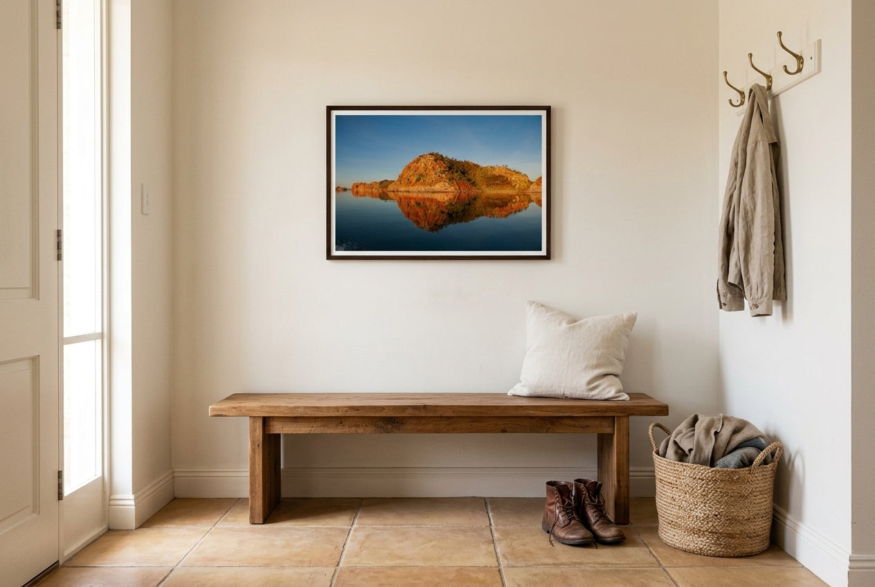 Golden Hour Mirror — Island Reflections, Lake Argyle, framed above a low recycled-timber bench in a quiet entry vestibule — cream linen cushion, leather boots, jute basket, dark wood frame. — Two Fat Bunnies.