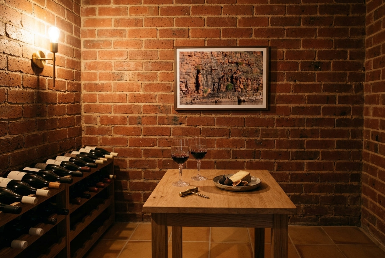 Golden Strata, Chamberlain Gorge, framed above a raw oak tasting table in a wine cellar tasting nook — exposed brick, corked bottles, warm sconce, dark wood frame. — Two Fat Bunnies.
