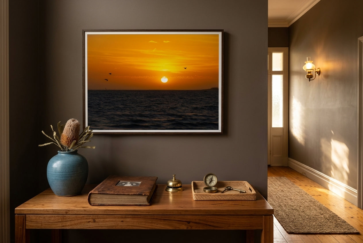 Golden Sunset Over Port Phillip Bay, framed above a generous blackbutt console in a Mornington heritage entry hall — deep mushroom plaster, coastal-blue ceramic, polished blackbutt floors, brass sconce, dark wood frame. — Two Fat Bunnies.