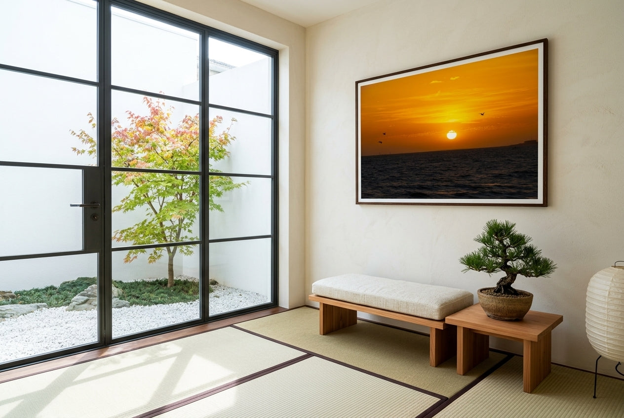 Golden Sunset Over Port Phillip Bay, framed in a Japanese-inspired garden room — floor-to-ceiling steel-framed glass door onto a dry-stone garden, low cedar bench, bonsai pine, paper lantern, dark wood frame. — Two Fat Bunnies.