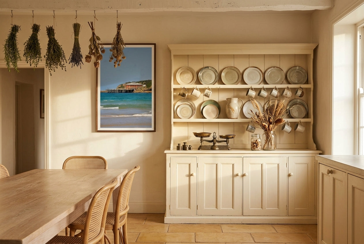 Heritage Tranquillity: Tathra Wharf, framed above a generous welsh dresser in a country Australian kitchen — hand-thrown ceramic plates, dried herbs hanging, vintage brass scales, dark wood frame. — Two Fat Bunnies.