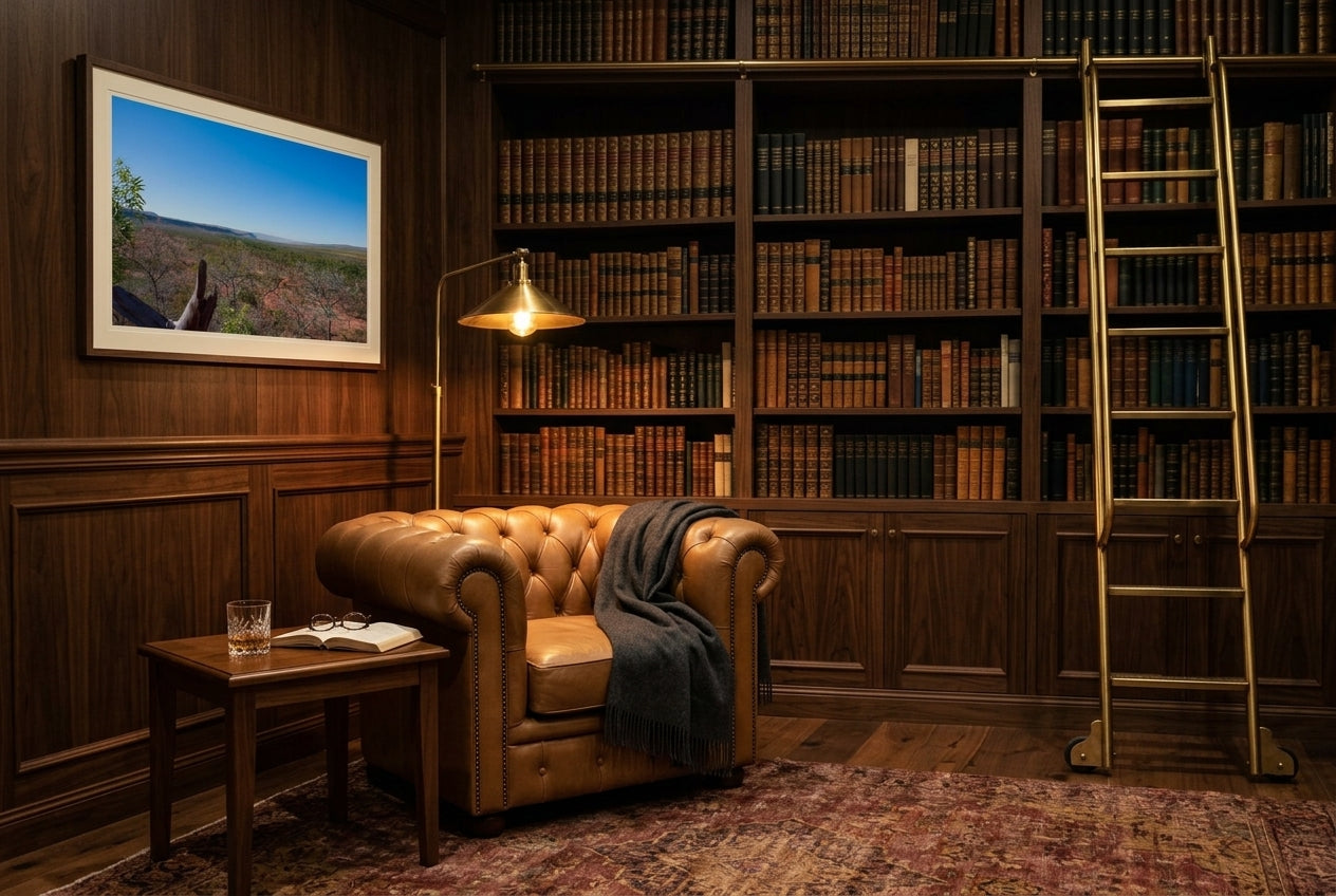 Kimberley Horizon — El Questro Lookout, framed in a literary library reading corner — leather Chesterfield armchair, floor-to-ceiling timber bookshelves, rolling library ladder, brass library lamp, dark wood frame. — Two Fat Bunnies.