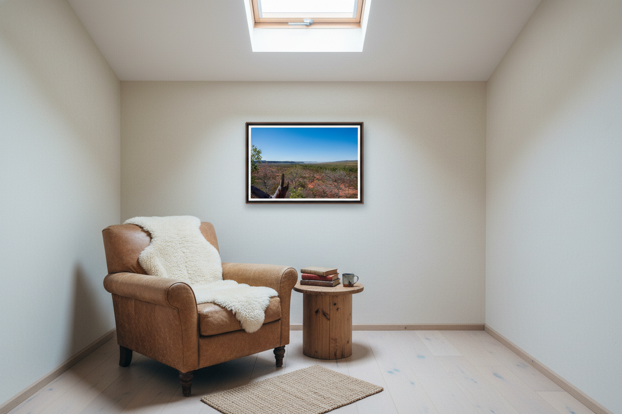 Kimberley Horizon — El Questro Lookout, framed in an elevated treetop reading lounge beneath a single skylight — low aged-leather lounge chair, sheepskin, side table, dark wood frame. — Two Fat Bunnies.