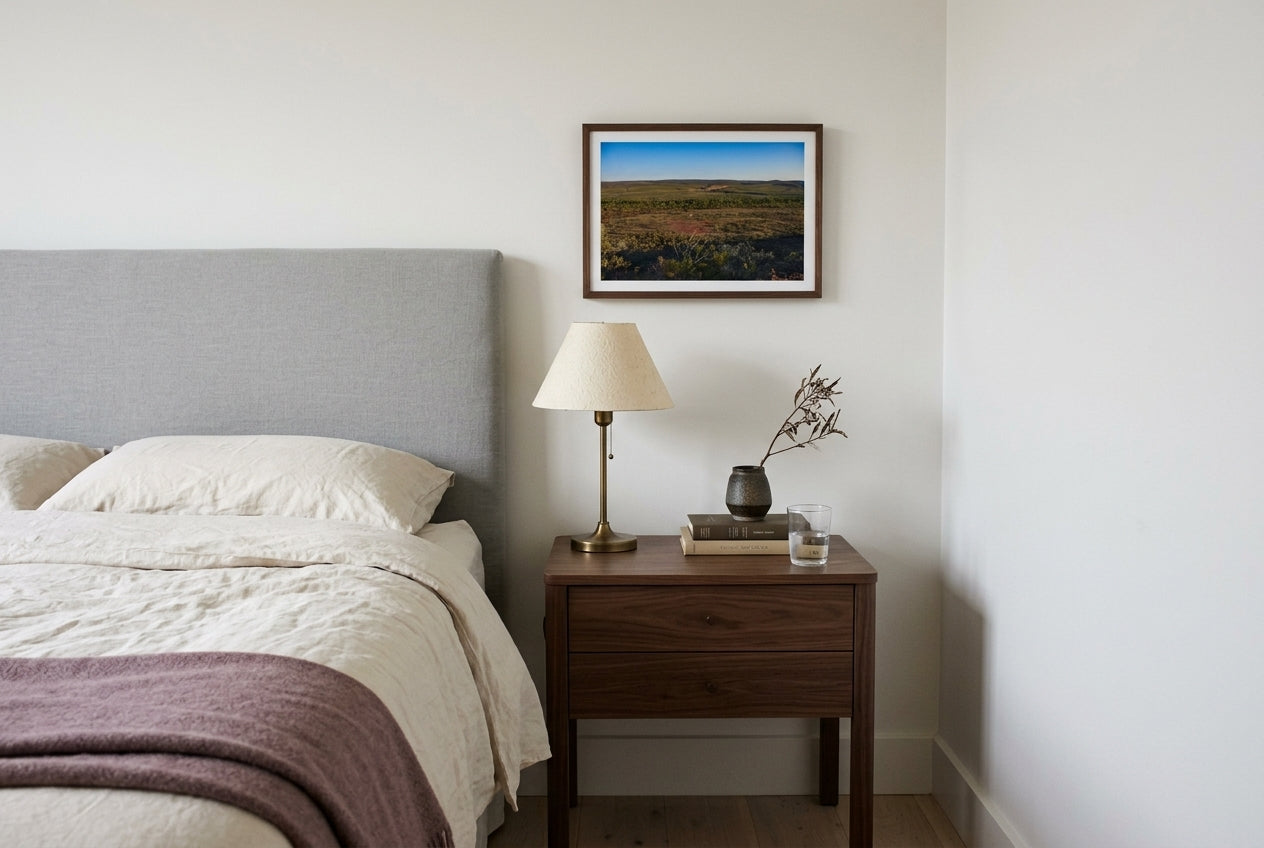 Late Light over El Questro, Buddy's Lookout, framed above a walnut bedside table in a Melbourne bedroom — dove-grey linen headboard, brass reading lamp, layered linen bedding, dark wood frame. — Two Fat Bunnies.