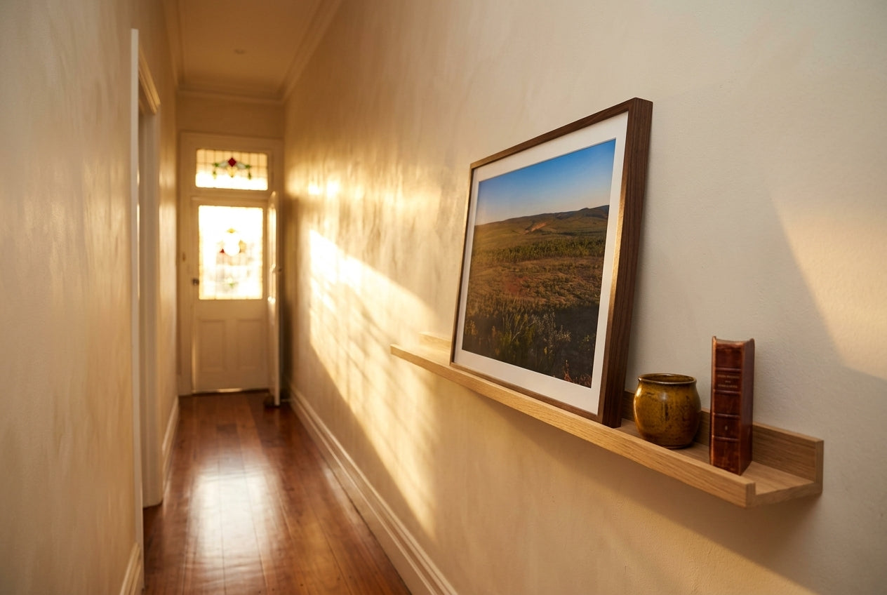Late Light over El Questro, Buddy's Lookout, propped on a slim oak picture ledge in a Melbourne terrace hallway — patterned ochre runner, dark spotted gum floor, ceramic vessel, book stop, dark wood frame. — Two Fat Bunnies.