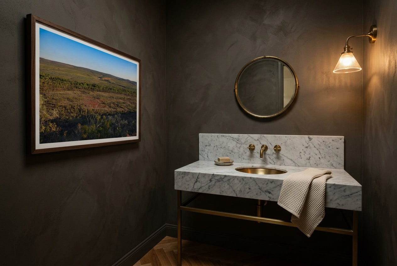Late Light over El Questro, Buddy's Lookout, framed as the sole artwork in a heritage Australian powder room — Carrara marble vanity, antique brass tap, deep mushroom-charcoal walls, warm sconce, dark wood frame. — Two Fat Bunnies.
