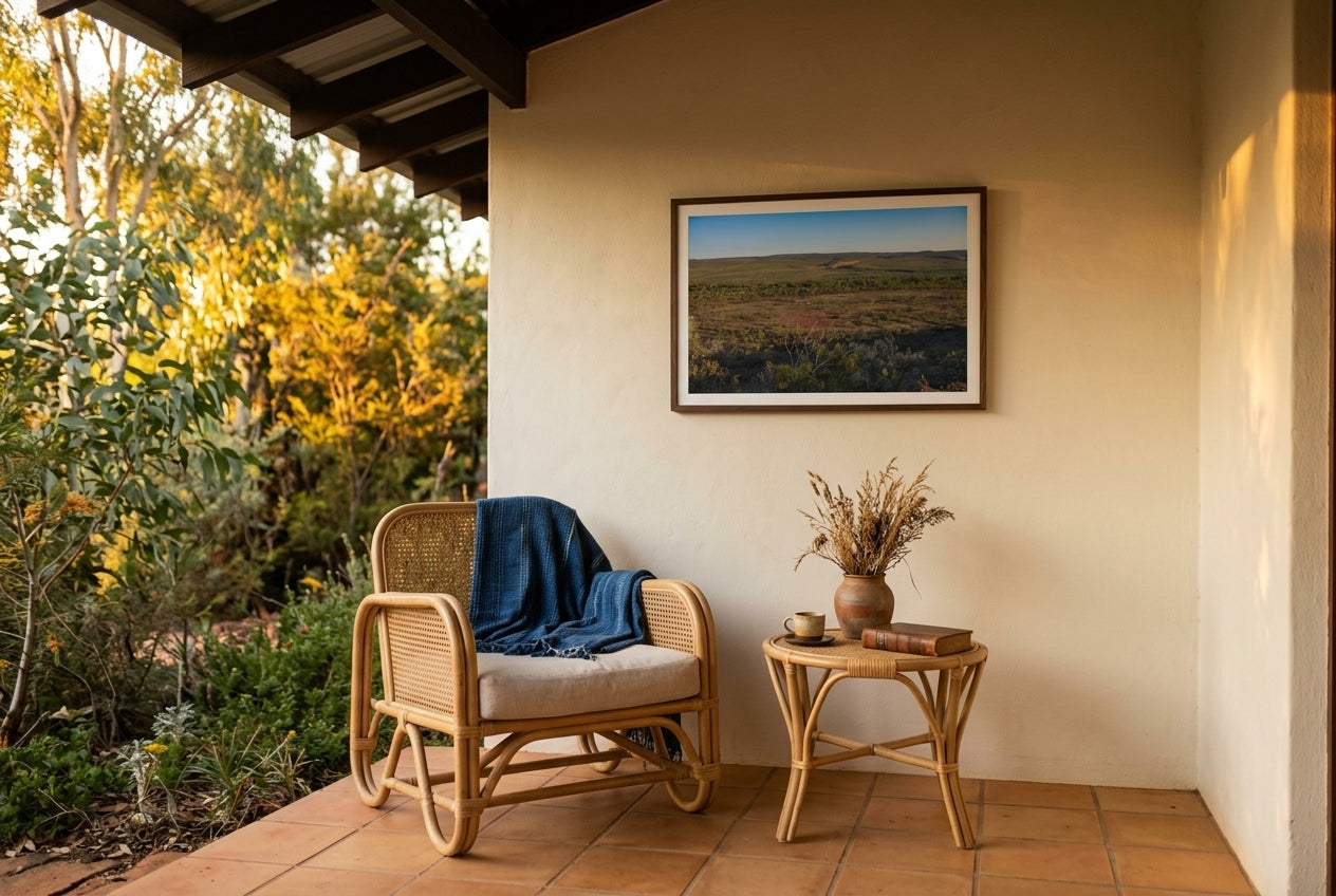 Late Light over El Questro, Buddy's Lookout, framed in a covered terrace seating corner — woven cane chair, pale linen cushion, bistro table with espresso and dried desert grasses, terracotta tile floor, dark wood frame. — Two Fat Bunnies.