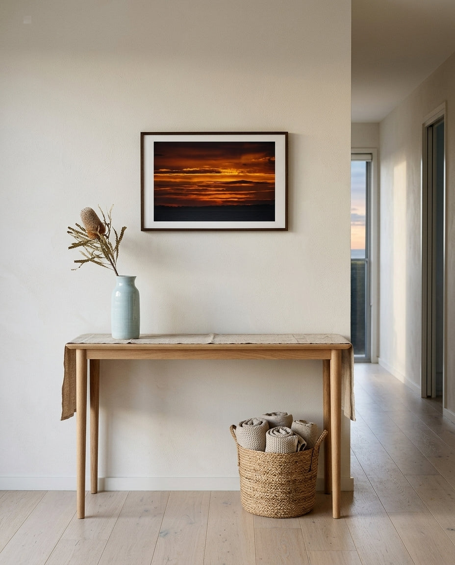 Sunrise over Bass Strait: Dawn at Flinders, framed along a beach house corridor — sisal runner, weatherboard panelling, brass wall sconce, woven driftwood mirror beyond, dark wood frame. — Two Fat Bunnies.