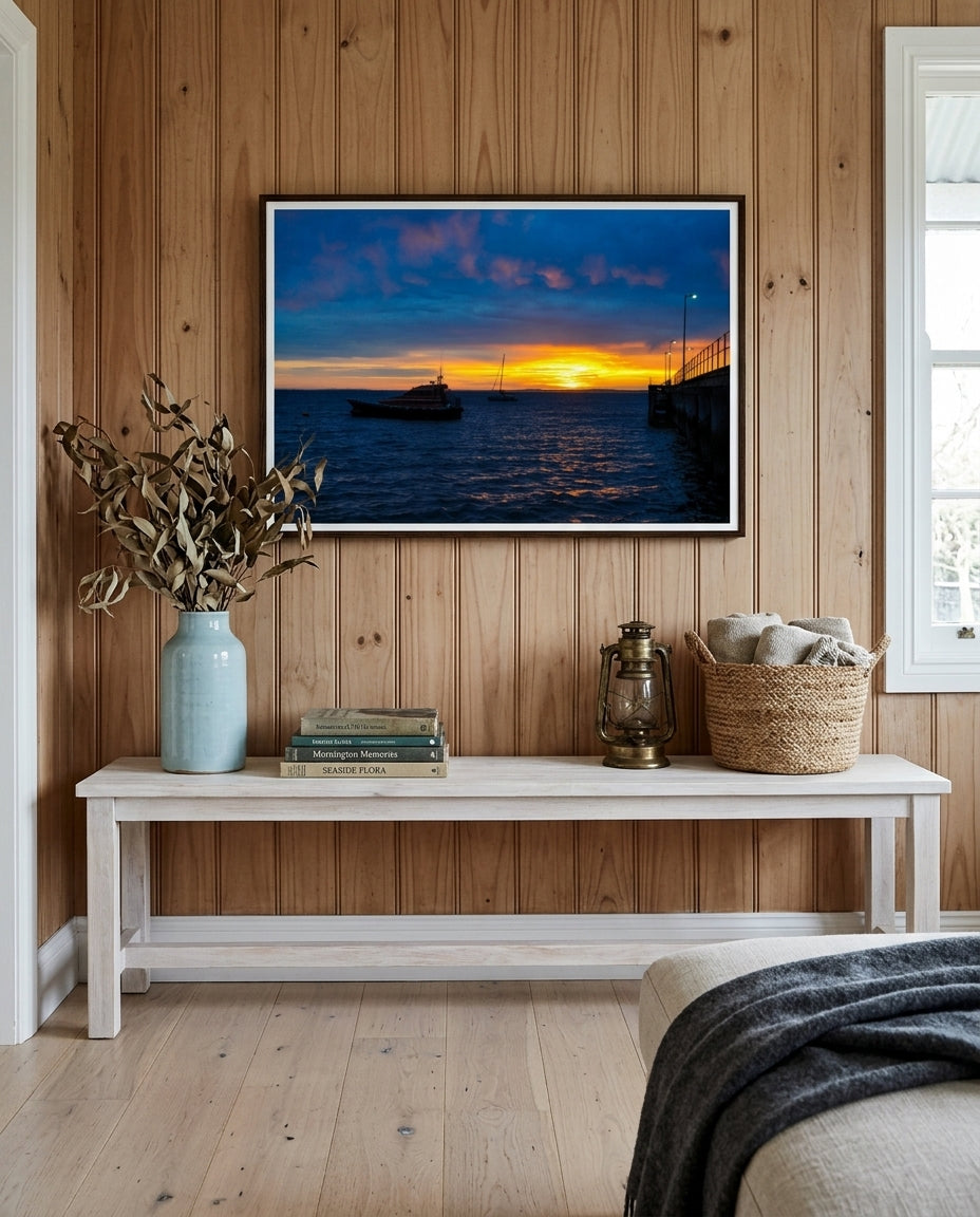 Sunrise Serenity at Flinders Pier, framed above a low blackbutt console in a weatherboard living room — limewash walls, ceramic vessel, woven cane lamp, photography books, dark wood frame. — Two Fat Bunnies.